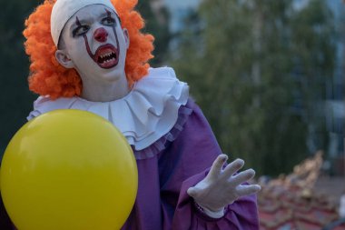 Cadılar bayramı, karnaval ya da parti için sokak kostümleri. Keskin dişli, korkunç palyaço kostümlü ve Azizler Günü tatili için sarı balonlu bir adam..