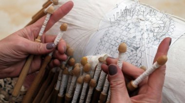 Zanaatkar kadın ince ipek ipliklerden güzel bir desen örüyor. El dokumacı Dantel. Dantel yastığın eski geleneği. Parmaklarının arasında bobinleri tutan kadın ellerinin yakın çekimi..