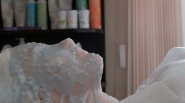 Kızın yüzü mavi aljinat bir maskeyle kaplı. Kozmetik ve sağlık. Spa prosedürü. Cilt tazeleme. Kamera sağdan sola hareket ediyor. Güzellik salonu..