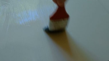 Yapıştırıcının üzerinde beyaz bir yonga üretim boyası için fırçayla yapıştırıcı uygulayan bir işçinin omzunun üzerinden bir manzara.