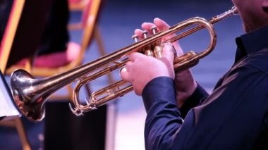 Siyah gömlekli bir adam trompet çalar. Erkek ellerine yakın çekim. Yan görüş. Adam senfoni orkestrasında müzisyen. Müzik konseri. Pirinç alet.