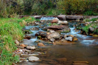 Tonto Creek Payson Arizona with small waterfall near background of forest and soft water effect flowing over the rocks. clipart