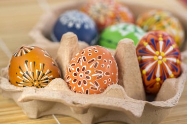 Group of painted Easter eggs in cardboard egg-box, Easter egg hunt celebration, colorful still life in paper box on light brown wooden background clipart