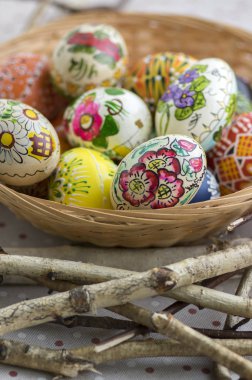 Kahverengi hasır sepet çiçek, ahşap kuş boyalı dallar, geleneksel Paskalya natürmort, renkli boyalı yumurta yuva