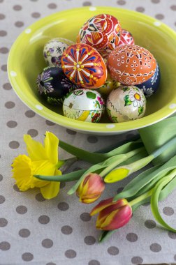 Grup balmumu Boyalı Paskalya yumurtaları yeşil benekli kase, kırmızı sarı laleler ve masa örtüsü lekeli sarı nergis çiçek açan çiçekler