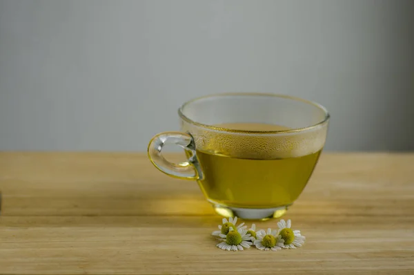 Matricaria chamomilla flowers and trasparent cup of tea on wooden table, fresh flowering herbal medicine in glass mug