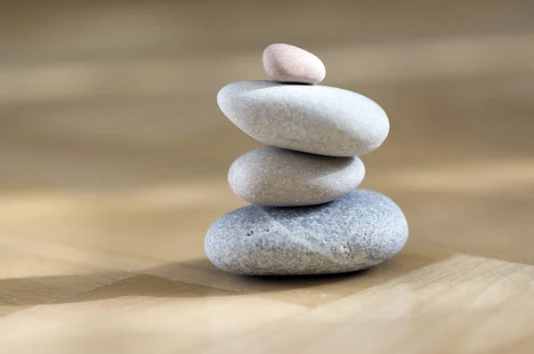 Group of zen stones pile, grey meditation pebbles tower on light brown wooden parquet background in sunlight