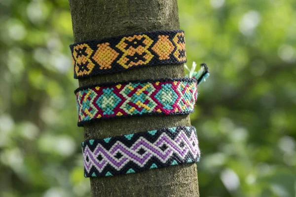 Natural bracelets of friendship on the tree branch, colorful woven friendship bracelets, green background, rainbow colors, checkered pattern, sunny