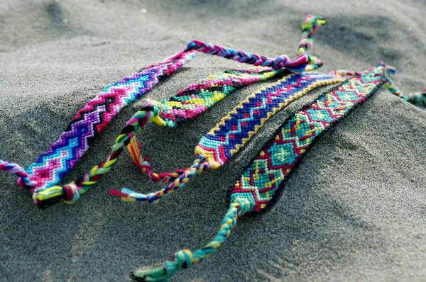 Natural bracelets of friendship in a row, colorful woven friendship bracelets, background, rainbow colors, checkered pattern, in the sand on the beach