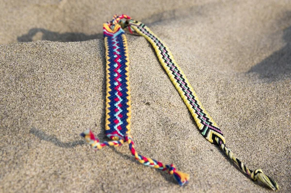 Natural bracelets of friendship in a row, colorful woven friendship bracelets, background, rainbow colors, checkered pattern, in the sand on the beach