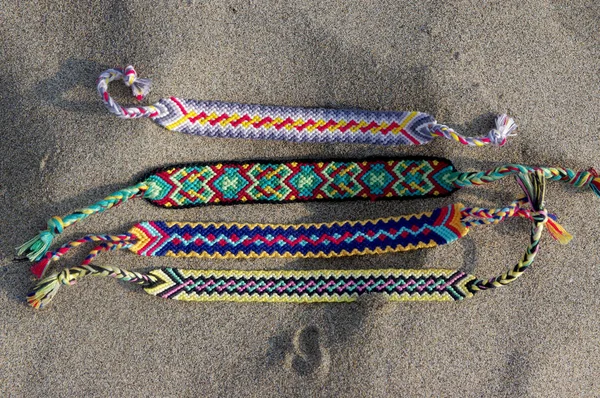 Natural bracelets of friendship in a row, colorful woven friendship bracelets, background, rainbow colors, checkered pattern, in the sand on the beach