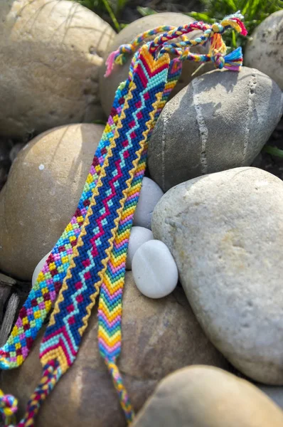 Natural bracelets of friendship in a row, colorful woven friendship bracelets, background, rainbow colors, checkered pattern, white pebbles