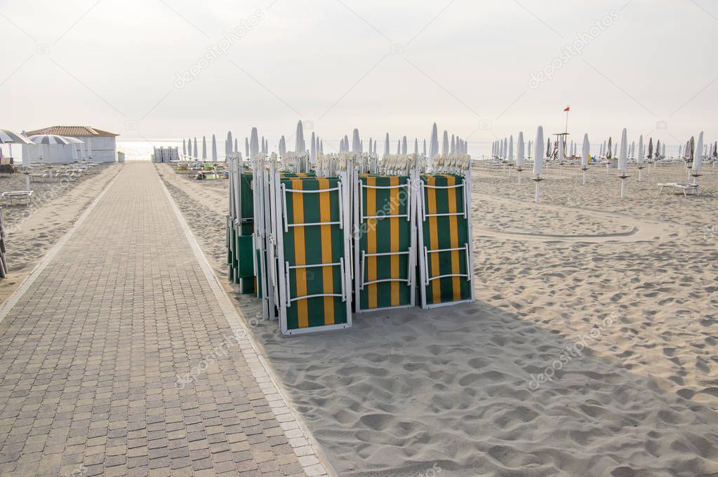 Beach with closed umbrellas and sunbeds, sun loungers and umbrellas, early morning in Sottomarina, Italy, Europe