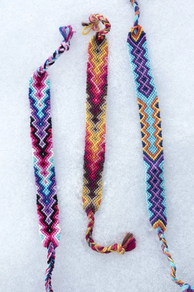 Natural bracelets of friendship in a row, colorful woven friendship bracelets in the white snow, background, rainbow colors