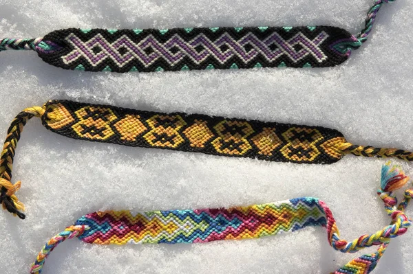 Natural bracelets of friendship in a row, colorful woven friendship bracelets in the white snow, background, rainbow colors