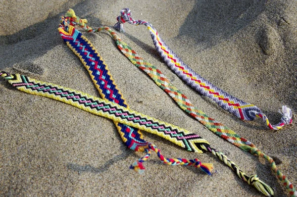 Natural bracelets of friendship in a row, colorful woven friendship bracelets, background, rainbow colors, checkered pattern, in the sand on the beach