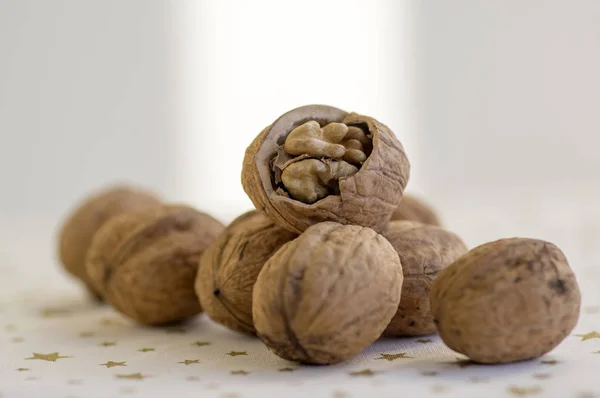 Walnuts in hard shells, pile on white Christmas tablecloth with golden stars, one nut with broken shell