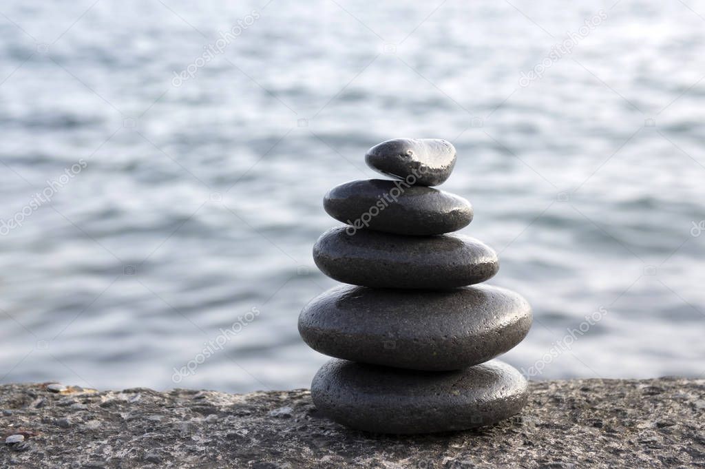 Five stones cairn tower, rock zen sculpture, black pebbles and ocean light blue background