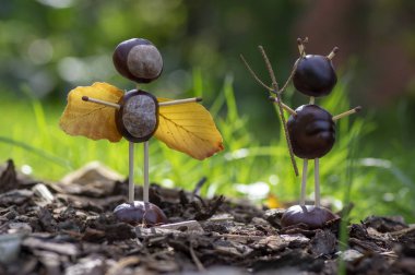 Melek ve şeytan figürleri sonbahar bahçesinde kestane, güvenlik kibritleri ve kuru yapraklardan yapılmıştır.