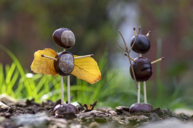 Melek ve şeytan figürleri sonbahar bahçesinde kestane, güvenlik kibritleri ve kuru yapraklardan yapılmıştır.