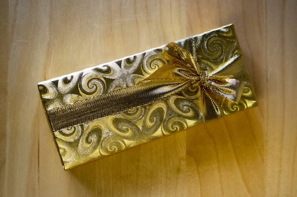 Golden gift box with golden ribbon on wooden background