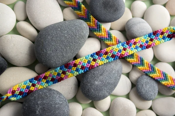 Natural bracelets of friendship in a row, colorful woven friendship bracelets, background, rainbow colors, checkered pattern, white and gray river stones