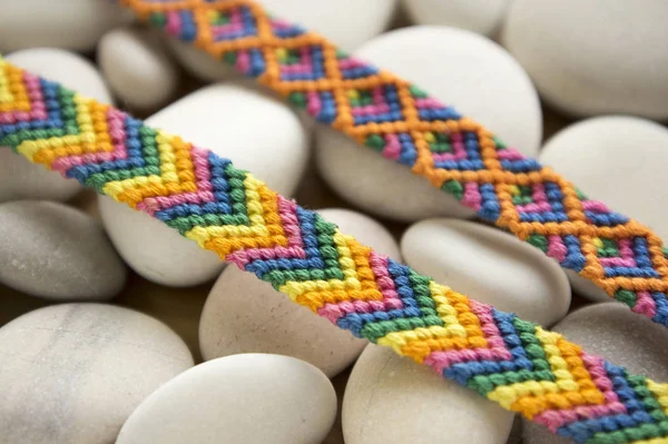 Bracelets of friendship, colorful woven friendship bracelets on white pebbles, white sea pebble stones, rainbow colors