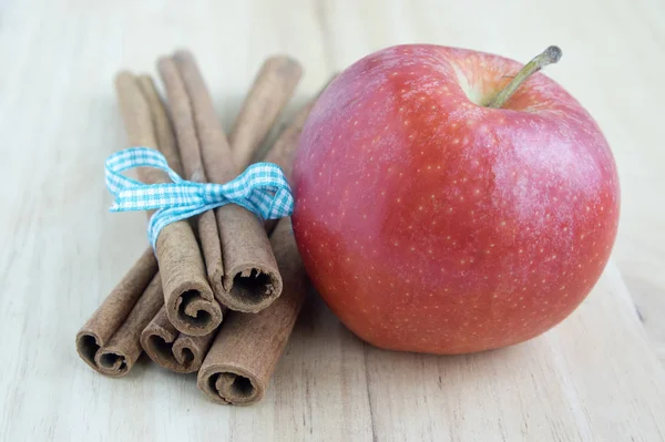 Fresh raw cinnamon sticks on wooden table tied with light blue checkered bow, one ripened red apple Gala