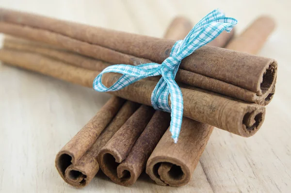 Fresh raw cinnamon sticks on wooden table tied with checkered bow