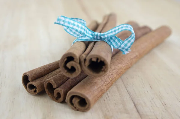 Fresh raw cinnamon sticks on wooden table tied with checkered bow
