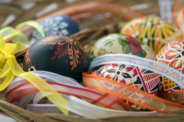 Цветные окрашенные пасхальные яйца в коричневую плетеную корзину, покрытую красочными лентами, традиционные пасхальные натюрморты
