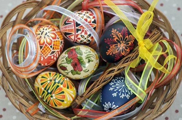 Colorful painted Easter eggs in brown wicker basket covered with colorful ribbons, traditional Easter still life