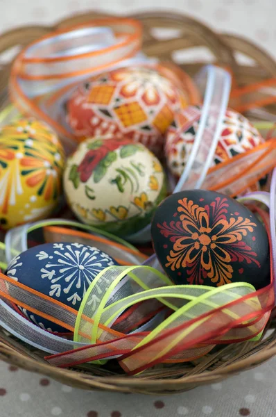 Цветные окрашенные пасхальные яйца в коричневую плетеную корзину, покрытую красочными лентами, традиционные пасхальные натюрморты — стоковое фото