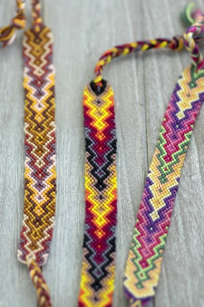 Tres coloridas pulseras tejidas naturales hechas a mano de amistad sobre fondo de madera, colores arco iris, patrón a cuadros — Foto de Stock