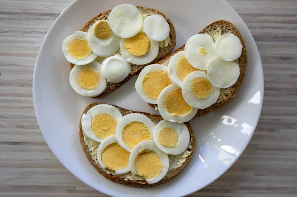 Açık ahşap masada beyaz tabak üzerinde tereyağı ile ortak çek ekmeği üzerinde dilimlenmiş haşlanmış yumurta