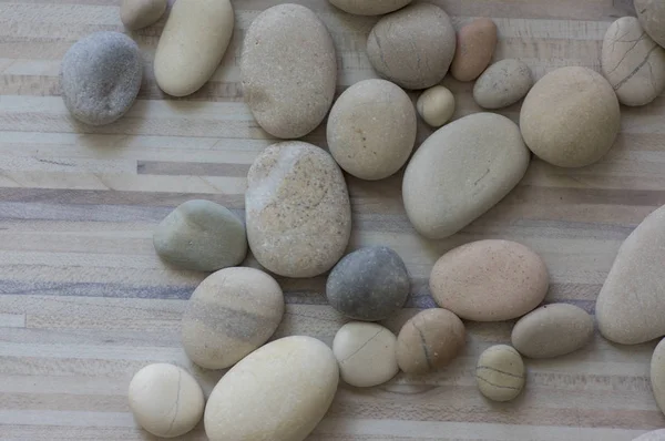 Gruppo di pietre bianche, grigie e marrone chiaro su fondo bianco in legno chiaro, spiaggia di ciottoli — Foto Stock