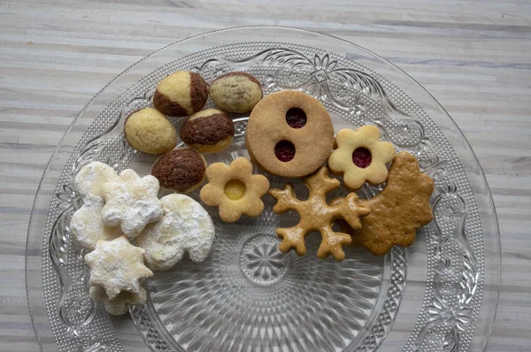 Many kinds of Christmas cookies on cut glass transparent plate, sweet food on wooden table — Stock Photo, Image