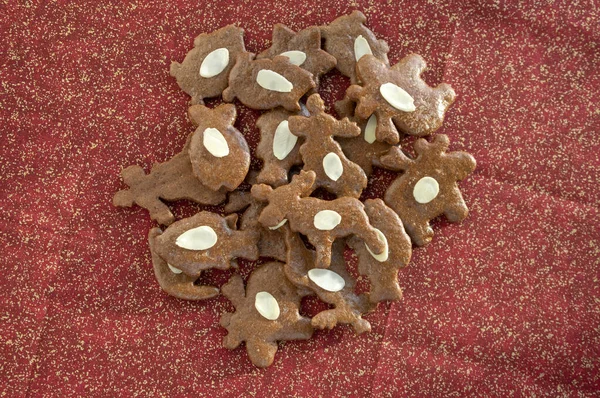 Brązowe morawskie ciemne pierniki z plasterkami migdałów, świąteczne ciasteczka na błyszczącym złotym czerwonym obrusie — Zdjęcie stockowe