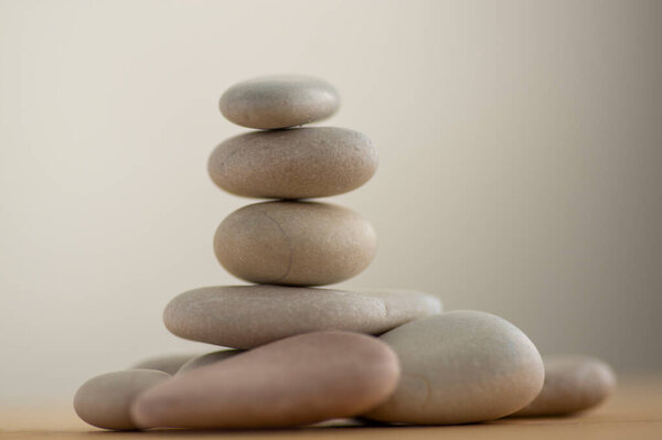 One simplicity stones cairn isolated on white background, group of light gray pebbles built in tower, wooden table, harmony and balance