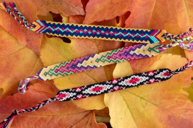 Sonbahar natürmortu, ev yapımı el yapımı renkli doğal örülmüş arkadaşlık bilezikleri kuru renk yaprakları üzerinde.