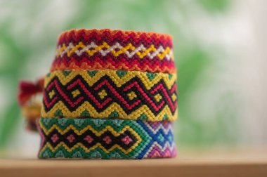 Üç el yapımı renkli doğal örgü bilezik açık ahşap arka planda izole edilmiş, gökkuşağı renkleri renkli, yeşil arkaplan