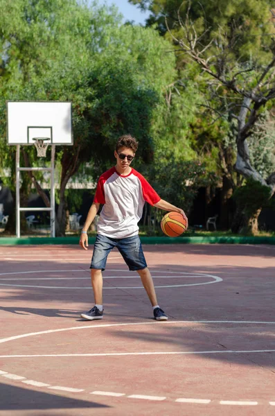 The boy is playing basketball alone in the basketball court.