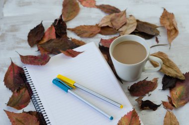 Sonbahar kavramı. Sonbahar yaprakları, kahve fincanı, defter ve renkli kalemler tahta masada vardır.