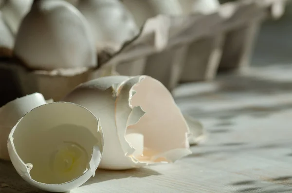 Close up of broken egg shells on wooden background,blurred background.There\'s a carton of eggs behind.