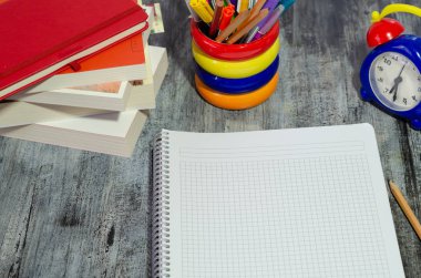 Ders kitapları, kalem, kurşun kalem, defter ve saat ahşap masaya vardır