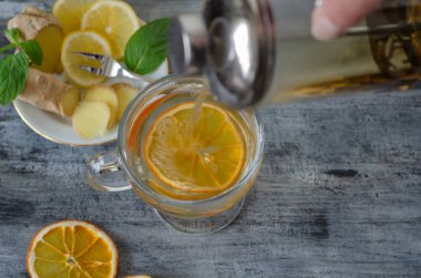 Bitkisel çay limon, zencefil, adaçayı, ıhlamur ve taze nane yaprakları ile. Kadın cama bitkisel çay doluyor.