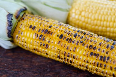 Ahşap bir masa üzerinde ızgara mısır koçanları.