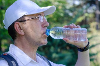 50'li yaşlardaki adam su içiyor.