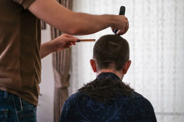 The young man is cutting  father\'s hair with hair clipper during coronavirus quarantine isolation at home .Home haircut concept.