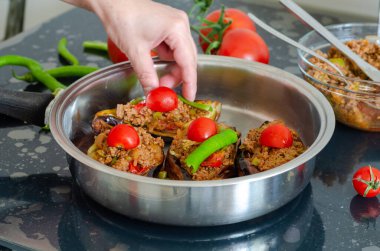 Kadın tavana patlıcan dolması (karniyarik) hazırlıyor. Kadın dolma patlıcanlara domates ve biber koyuyor.